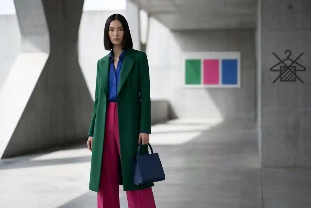 Color blocking — jak łączyć kolory kontrastowe w stylizacji? Modelka ubrana w stylizację ukazującą główne zasady color blockingu, składającą się z gładkich, jednolitych materiałów: dominujących szmaragdowych spodni, kobaltowego topu oraz fuksjowej torebki jako akcentu.